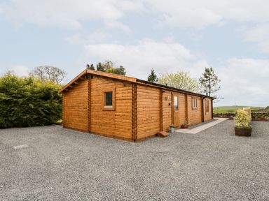 A wooden cabin with gravel surroundings and some plants near Howgill Lodge in Gatebeck near Kirkby Lonsdale