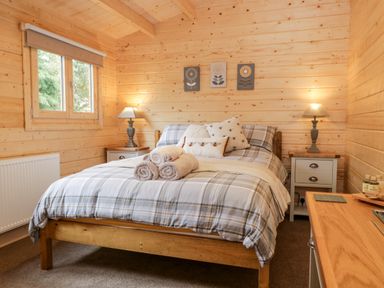 A bedroom with a plaid bedspread wooden walls lamps on bedside tables and rolled towels on the bed at Howgill Lodge in Gatebeck near Kirkby Lonsdale