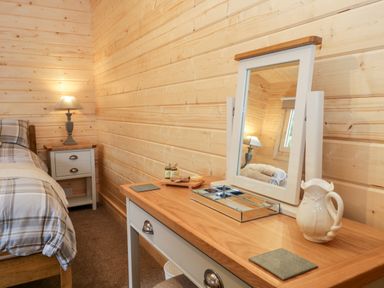 A bedroom with a wooden dressing table and mirror next to a bedside table with a lamp at Howgill Lodge in Gatebeck near Kirkby Lonsdale