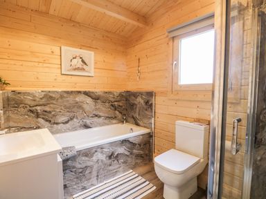 A bathroom with a bathtub a toilet a sink a window and a shower at Howgill Lodge in Gatebeck near Kirkby Lonsdale