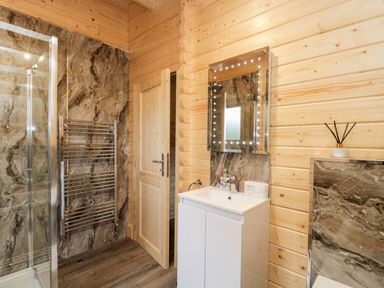 A bathroom with a shower, towel rack, wooden door, sink with cabinet, and LED mirror at Howgill Lodge in Gatebeck near Kirkby Lonsdale