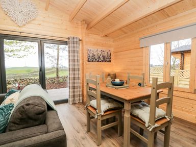 A dining area with a wooden table and chairs next to a sofa and large glass doors at Howgill Lodge in Gatebeck near Kirkby Lonsdale