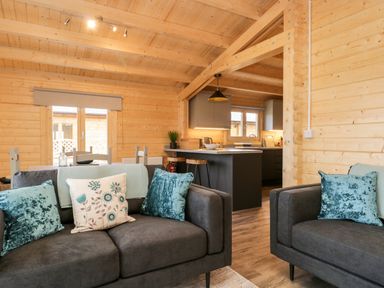 A living area with two gray sofas with cushions and a kitchen with an island and stools at Howgill Lodge in Gatebeck near Kirkby Lonsdale