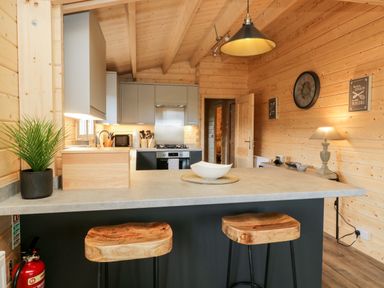 A kitchen with wooden stools a countertop a plant and a clock on the wall at Howgill Lodge in Gatebeck near Kirkby Lonsdale