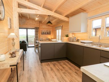 A kitchen with dark cabinets a sink and toaster next to a dining area with chairs and a table at Howgill Lodge in Gatebeck near Kirkby Lonsdale