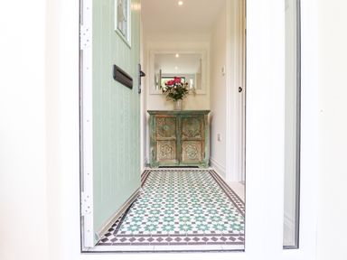 An entryway with a green door a patterned tile floor a distressed wooden cabinet with flowers and a mirror at Bluebell Cottage in Mary Tavy