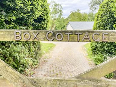 A wooden gate with Box Cottage sign with a paved driveway and greenery behind at Bluebell Cottage in Mary Tavy