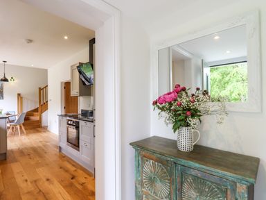 A hallway with a floral arrangement on a wooden cabinet and a kitchen and dining area with wooden floors at Bluebell Cottage in Mary Tavy