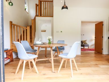 A dining area with a round wooden table surrounded by four gray chairs next to a wooden staircase at Bluebell Cottage in Mary Tavy