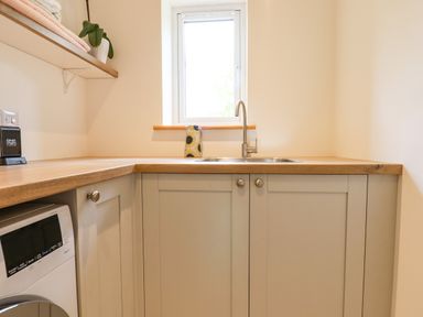A kitchen corner with a wooden countertop a stainless steel sink a window grey cabinets and a washing machine at Bluebell Cottage Mary Tavy