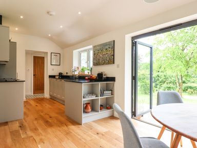A kitchen with gray cabinets wooden floor and an open door leading outside at Bluebell Cottage in Mary Tavy