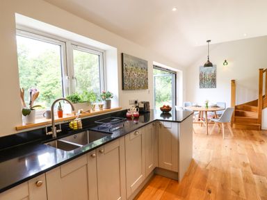 A kitchen with black countertops plants on the windowsill and a dining area with a round wooden table and chairs at Bluebell Cottage in Mary Tavy