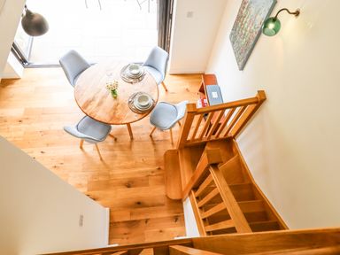 A dining area with a round wooden table and four light grey chairs next to wooden stairs and a wall light at Bluebell Cottage in Mary Tavy