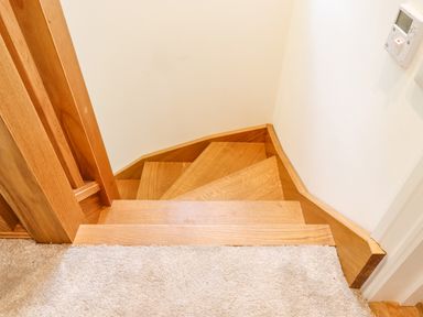 A wooden spiral staircase with beige carpeted floor and white walls at Bluebell Cottage in Mary Tavy