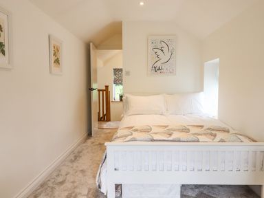 A bedroom with a white bed and quilt two framed pictures on the side wall and a framed dove picture above the bed at Bluebell Cottage in Mary Tavy