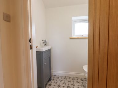 A small bathroom with a gray vanity unit and a window at Bluebell Cottage in Mary Tavy