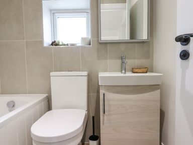A bathroom with a toilet next to a sink cabinet and a small window above at Bluebell Cottage in Mary Tavy