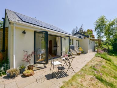 A patio with a small table and chairs outside a single story house with solar panels on the roof at Bluebell Cottage in Mary Tavy