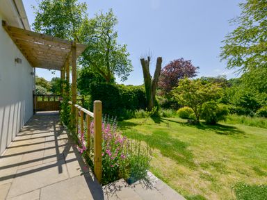 A garden with grass trees and flowers next to a house with a wooden pergola at Bluebell Cottage in Mary Tavy