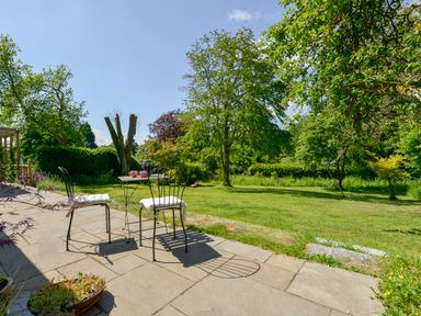 A garden patio with two metal chairs and a table surrounded by grass and trees at Bluebell Cottage in Mary Tavy