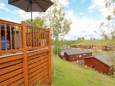A wooden deck with umbrella overlooking several wooden cabins on a grassy hill at Rashierigg in Catterick North Yorkshire
