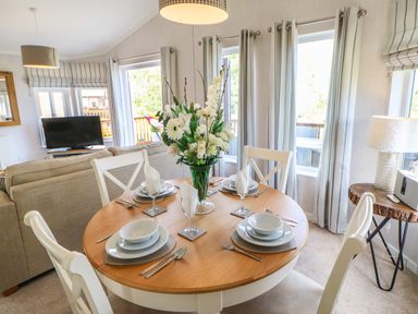 A dining area with a round wooden table set for four and a living area with a sofa and television at Rashierigg in Catterick North Yorkshire