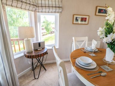 A dining area with a round wooden table set with dishes and cutlery next to a small wooden side table with a lamp and speaker at Rashierigg in Catterick North Yorkshire