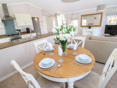 A dining area with a round wooden table set with plates glasses and cutlery a kitchen and living room in the background at Rashierigg in Catterick North Yorkshire