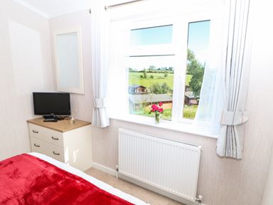 A bedroom with a red blanket on the bed a chest of drawers with a television and a vase with flowers on the windowsill at Rashierigg in Catterick North Yorkshire