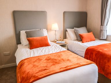 A bedroom with two single beds with orange blankets and pillows and a nightstand with a lamp at Rashierigg in Catterick North Yorkshire