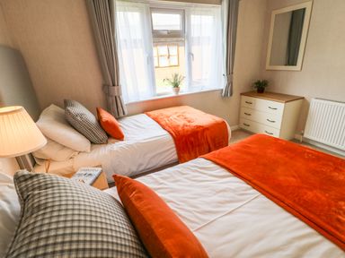 A bedroom with two single beds with orange blankets and pillows a window with curtains a lamp a dresser with a mirror and a plant at Rashierigg in Catterick North Yorkshire