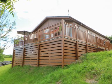 A wooden deck with railing and umbrella attached to a house on a grassy hill at Rashierigg in Catterick North Yorkshire
