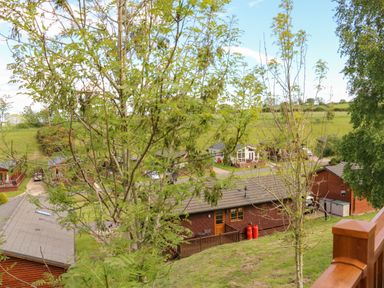 A view of wooden lodges behind trees and a grassy hill at Rashierigg in Catterick North Yorkshire