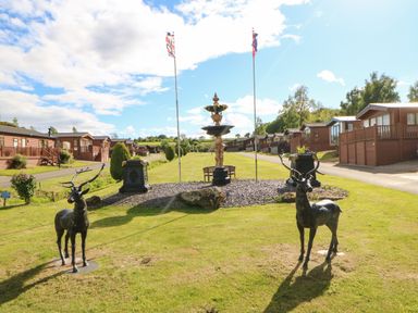 An outdoor area with two deer statues a central fountain flagpoles and wooden lodges at Rashierigg in Catterick North Yorkshire