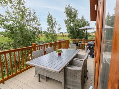 An outdoor deck with a dining table and chairs a small round table with chairs and an umbrella and a grill at Rashierigg in Catterick North Yorkshire