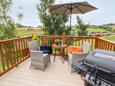 An outdoor balcony with two chairs a small table with drinks an umbrella and a barbecue grill at Rashierigg in Catterick North Yorkshire