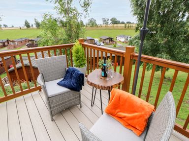 A balcony with two chairs with cushions and blankets a wooden table with a bottle and glasses and a potted plant at Rashierigg in Catterick North Yorkshire