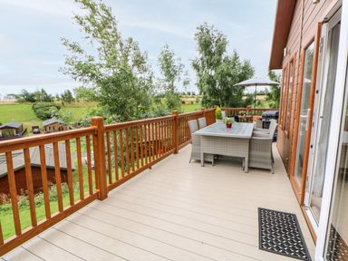 An outdoor deck with a wooden railing patio table and chairs plants and a grill at Rashierigg in Catterick North Yorkshire