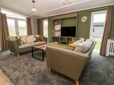 A living room with two sofas a coffee table a television on a stand and windows with curtains at Lily in Broadwoodwidger near Ashwater