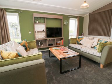 A living room with two sofas a wooden coffee table and a wall-mounted television at Lily in Broadwoodwidger near Ashwater