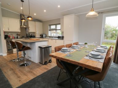 A kitchen with island and bar stools next to a dining table set with plates and glasses at Lily Broadwoodwidger near Ashwater