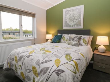 A bedroom with a bed featuring leaf patterned bedding two bedside tables with lamps and a window at Lily in Broadwoodwidger near Ashwater
