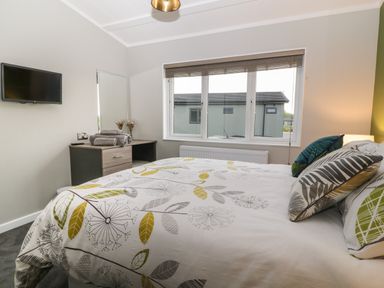 A bedroom with a double bed a dresser with towels and a TV mounted on the wall at Lily in Broadwoodwidger near Ashwater