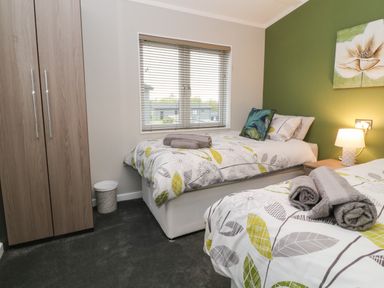 A bedroom with two single beds with patterned bedding a wooden wardrobe and a window at Lily Broadwoodwidger near Ashwater
