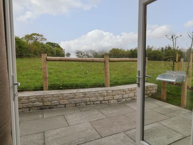 A patio area with stone paving and a low brick wall overlooking a grassy field at Lily in Broadwoodwidger near Ashwater