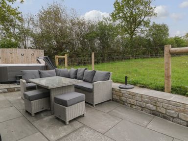 An outdoor patio with a grey cushioned wicker sofa set and a hot tub in a fenced garden at Lily Broadwoodwidger near Ashwater