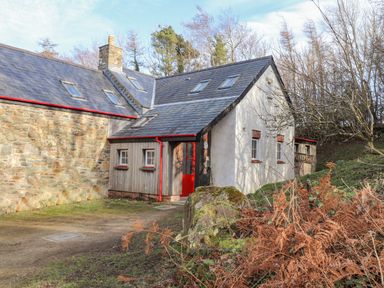 A stone and white plaster house with red door and window frames surrounded by trees and shrubs at Pen y Mynydd in Newport Pembrokeshire