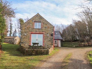 A stone house with picnic table in front on a grassy area next to a dirt driveway at Pen y Mynydd in Newport Pembrokeshire