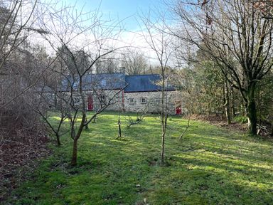 A garden with small trees and grass in front of a stone house with a slate roof and red doors at Pen y Mynydd in Newport Pembrokeshire