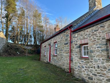 A stone cottage with red window frames and door in a grassy area with trees in the background at Pen y Mynydd in Newport Pembrokeshire